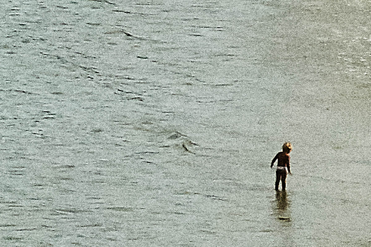 The blurred silhouettes of a child playing at the water's edge on a beach in Brittany in the summer, from the series Another summer by Emmanuel Pineau