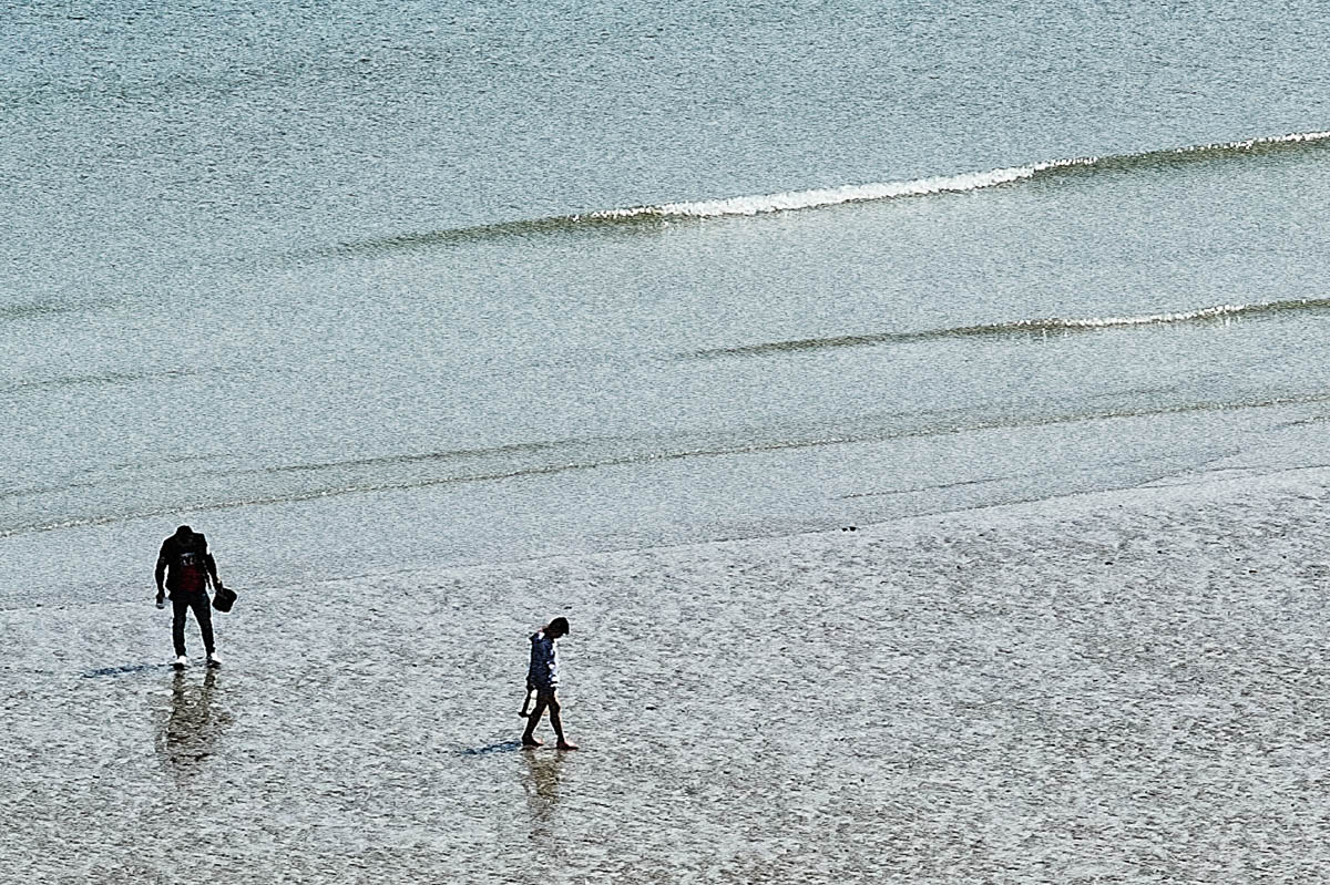 The blurred silhouettes of two men searching for seashells at the water's edge on a beach in Brittany in the summer, from the series Another summer by Emmanuel Pineau