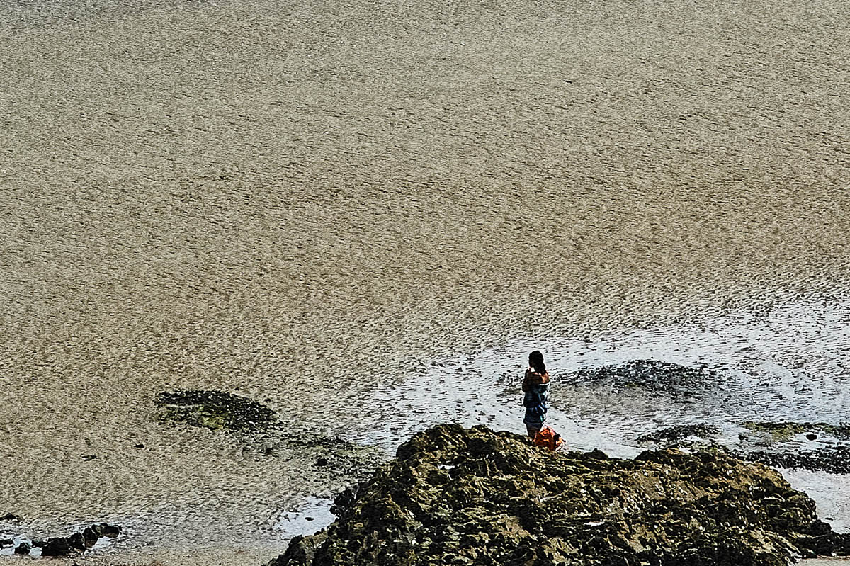 The blurred silhouette of a young woman changing clothes near the rocks on a beach in Brittany in the summer, from the series Another summer by Emmanuel Pineau