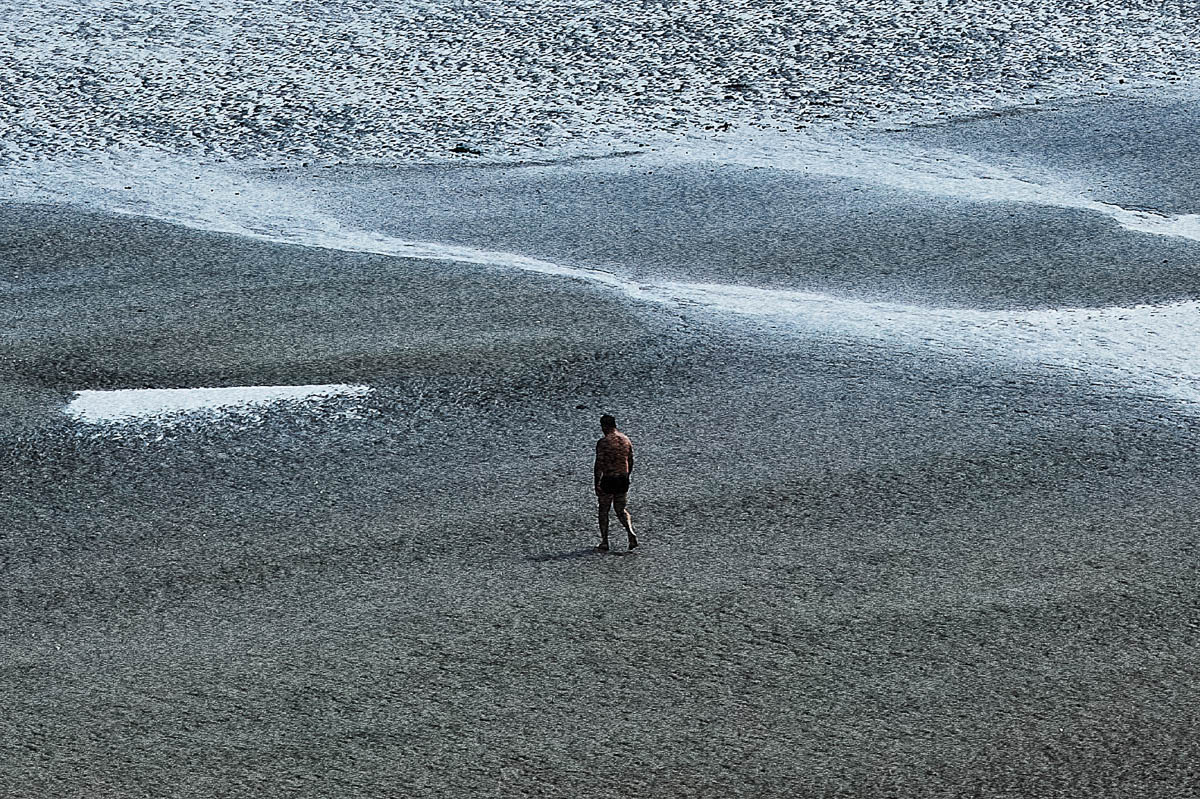 The blurred silhouette of a man walking towards the sea on a beach in Brittany in summer, from the series Another summer by Emmanuel Pineau