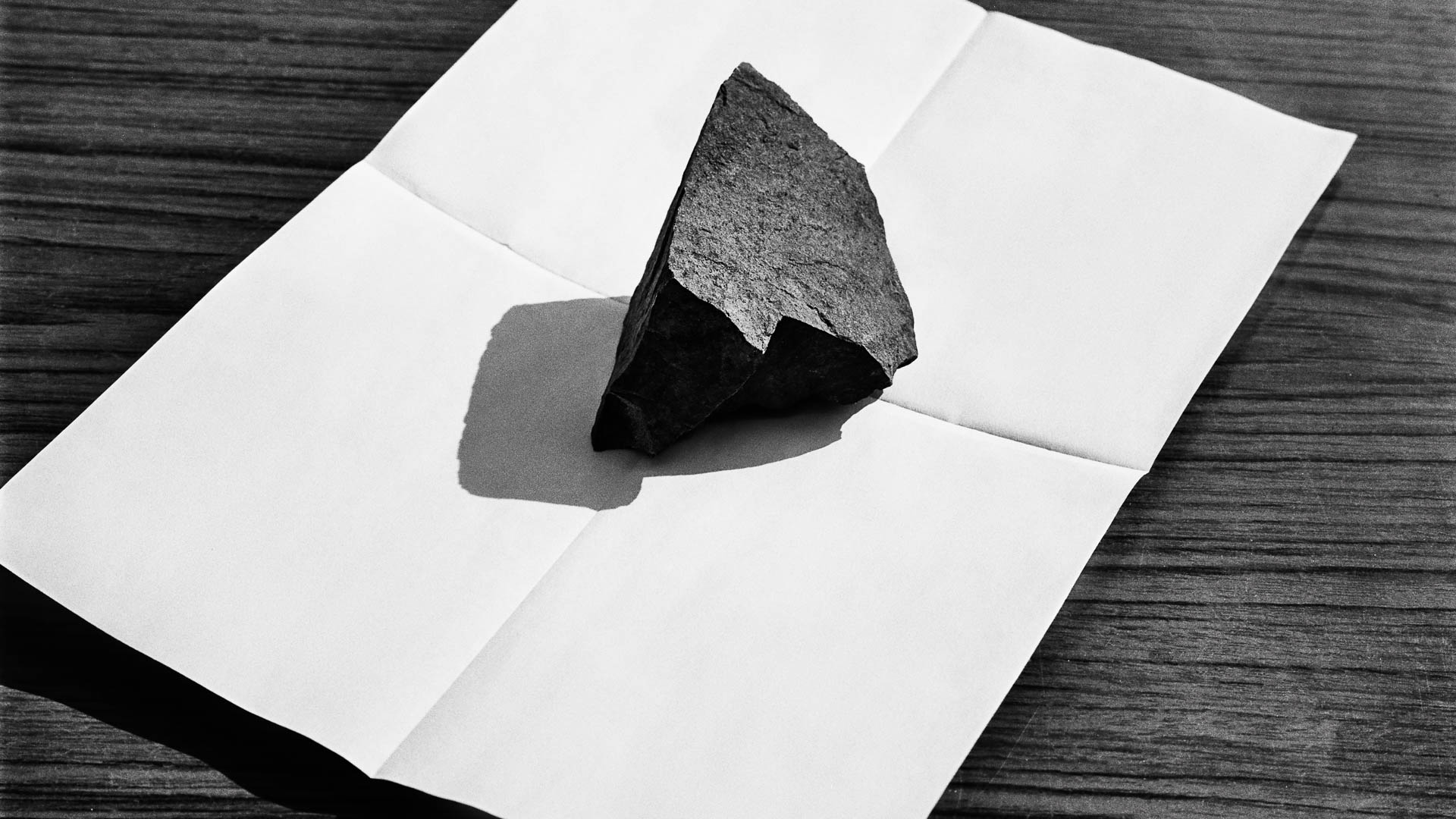 A stone is placed on a sheet of white paper, from the series One piece of my mind by Emmanuel Pineau