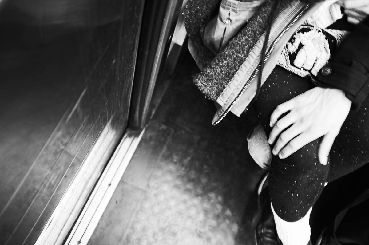 A man's hand resting on his partner's knee on the Paris metro, from the series Going Underground by Emmanuel Pineau