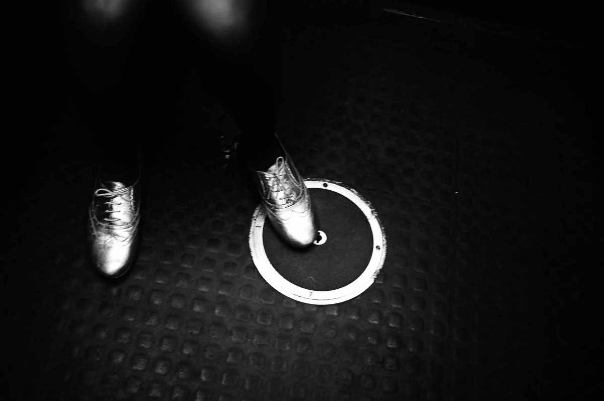 Close-up of a woman's legs wearing black tights and silver shoes, from the series Going Underground by Emmanuel Pineau
