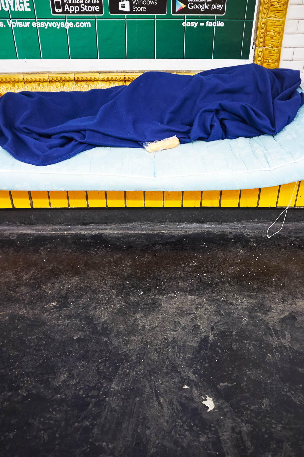 A man sleeps in a blue sleeping bag on a subway platform in Paris, from the series Going Underground by Emmanuel Pineau