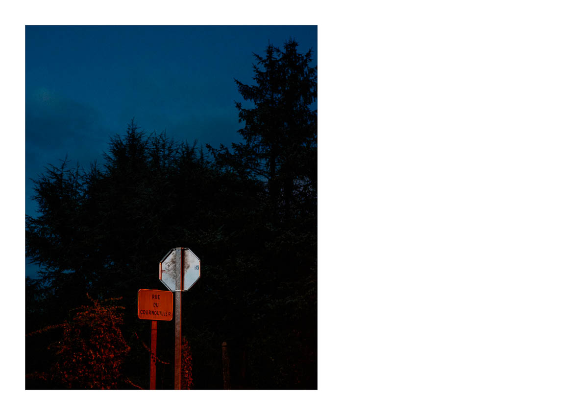 Road signs in a village in Normandy at dusk, from the series I will be around by Emmanuel Pineau