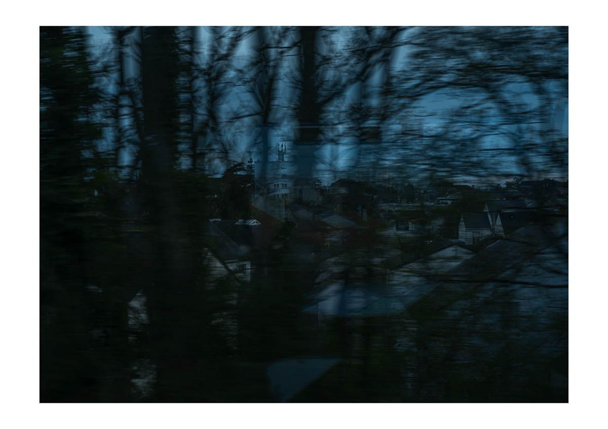Blurry trees in front of the city, seen from the moving train arriving in Cholet. From the series I will be around by Emmanuel Pineau