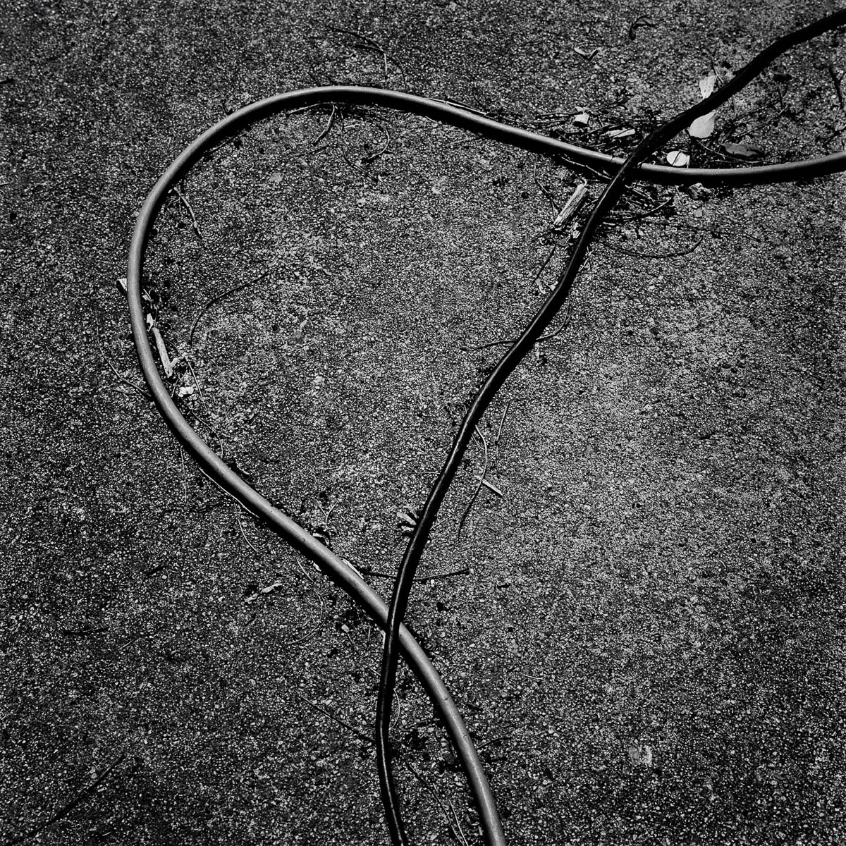 Abstract composition with two garden hoses on the ground, from the series Les limites du territoire by Emmanuel Pineau