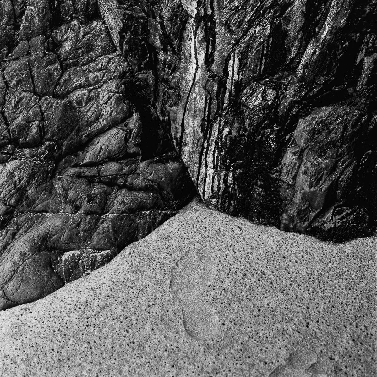Footprints in the sand at the foot of the granite cliffs in Brittany, from the series Les limites du territoire by Emmanuel Pineau