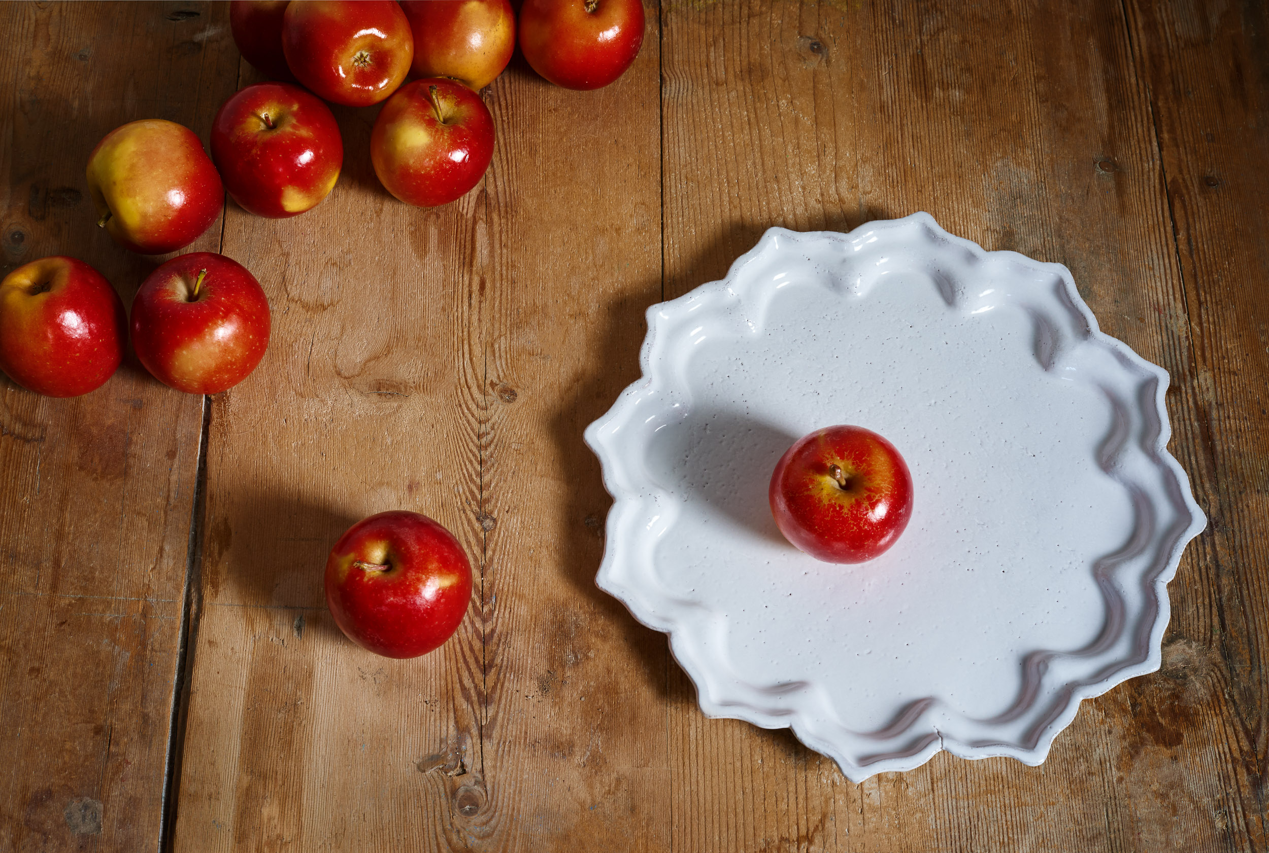 Large white ceramic platter by Astier de Villatte on a rustic wooden table with red apples, still life photography by Emmanuel Pineau
