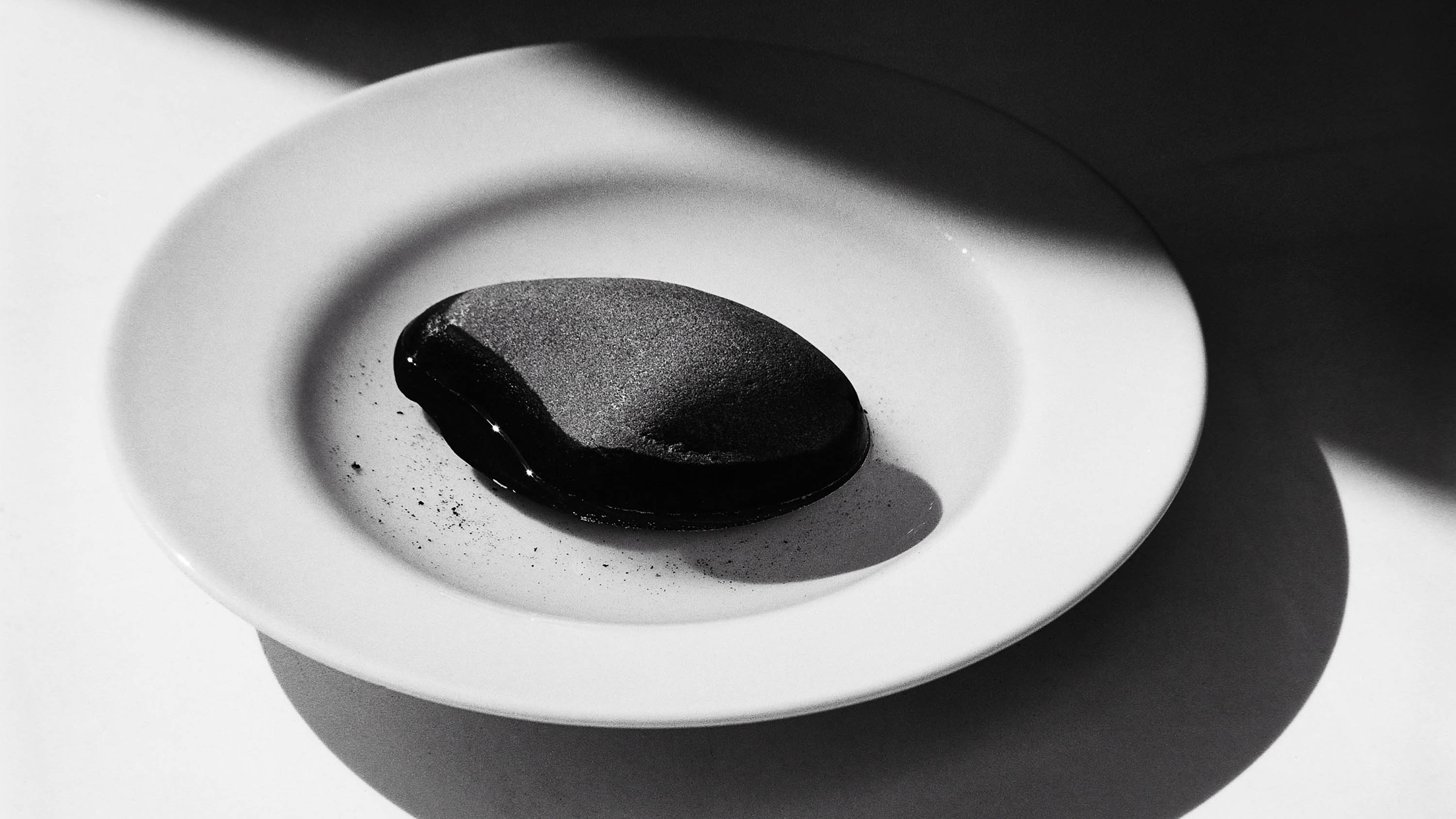 A large black pebble placed on a white plate, from the series A simple life, by Emmanuel Pineau