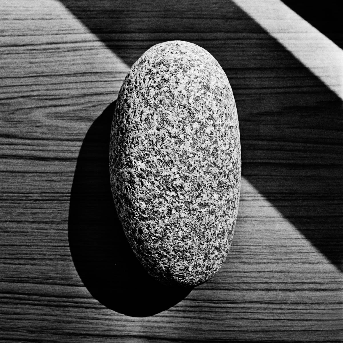 A large granite pebble placed on a wooden table in the late afternoon sun, from the series One piece of my mind by Emmanuel Pineau