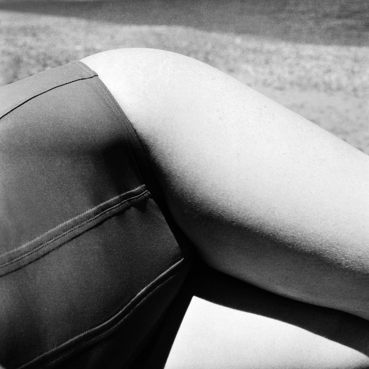 Close-up of the hips of a woman in a swimsuit lying on a beach, from the series One piece of my mind by Emmanuel Pineau