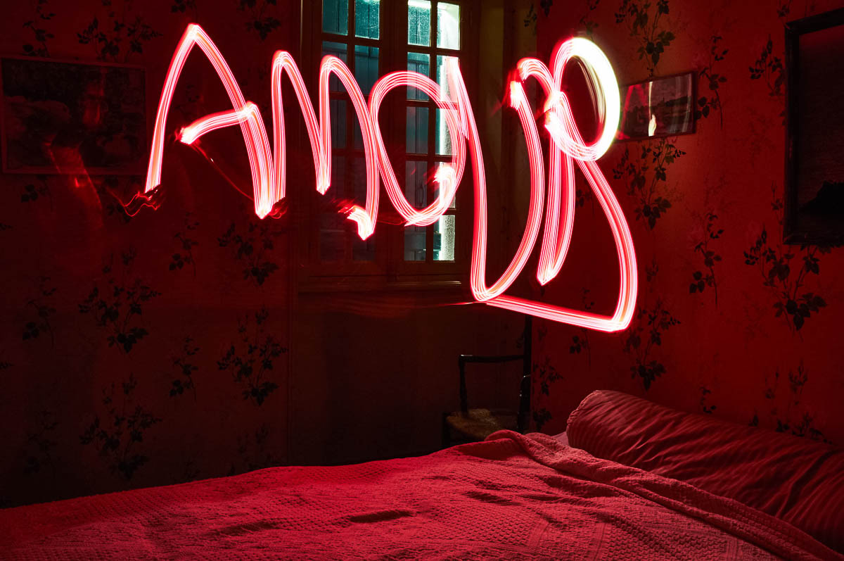 Vintage bedroom with the word LOVE written in red light painting above the bed, from the series Out of disorders by Emmanuel Pineau