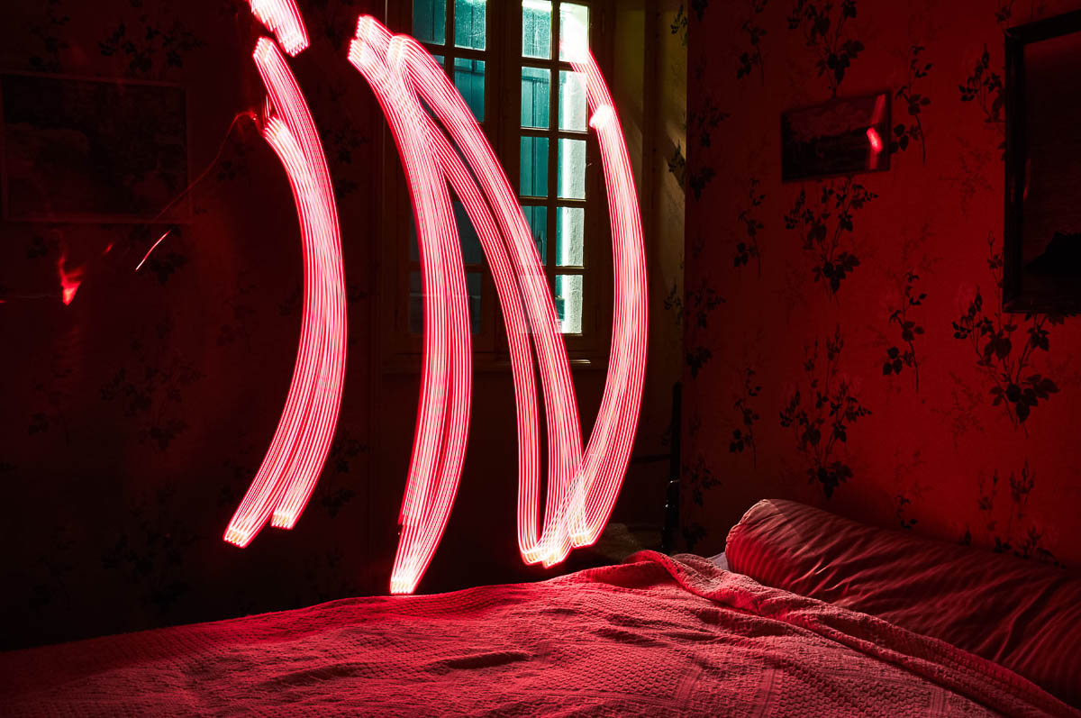 Vintage bedroom with the word IN written in red light painting above the bed, from the series Out of disorders by Emmanuel Pineau