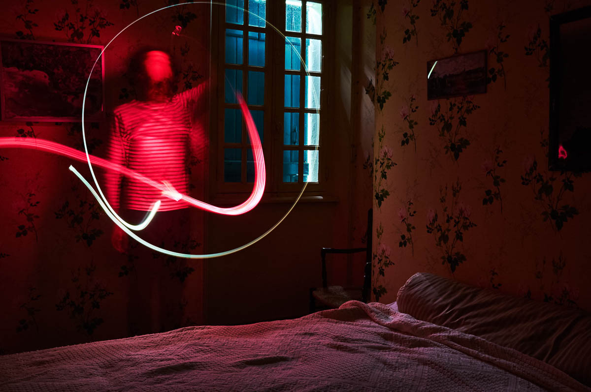 Self-portrait of Emmanuel Pineau in a vintage bedroom with a red light painting effect, from the series Out of disorders by Emmanuel Pineau