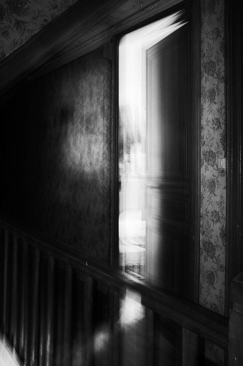 View of a dark hallway in a vintage house with a half-open door, from the series Out of disorders by Emmanuel Pineau