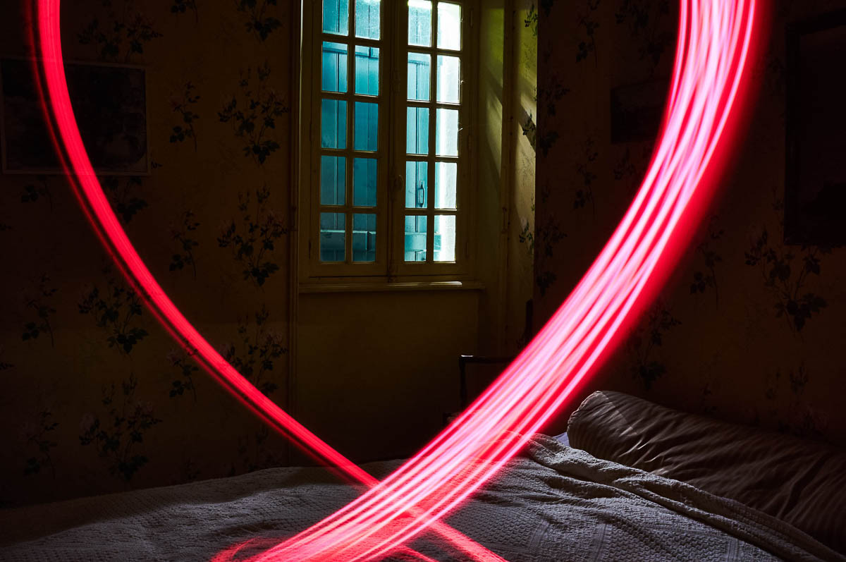 A bedroom in semi-darkness with a red light painting effect, from the series Out of disorders by Emmanuel Pineau