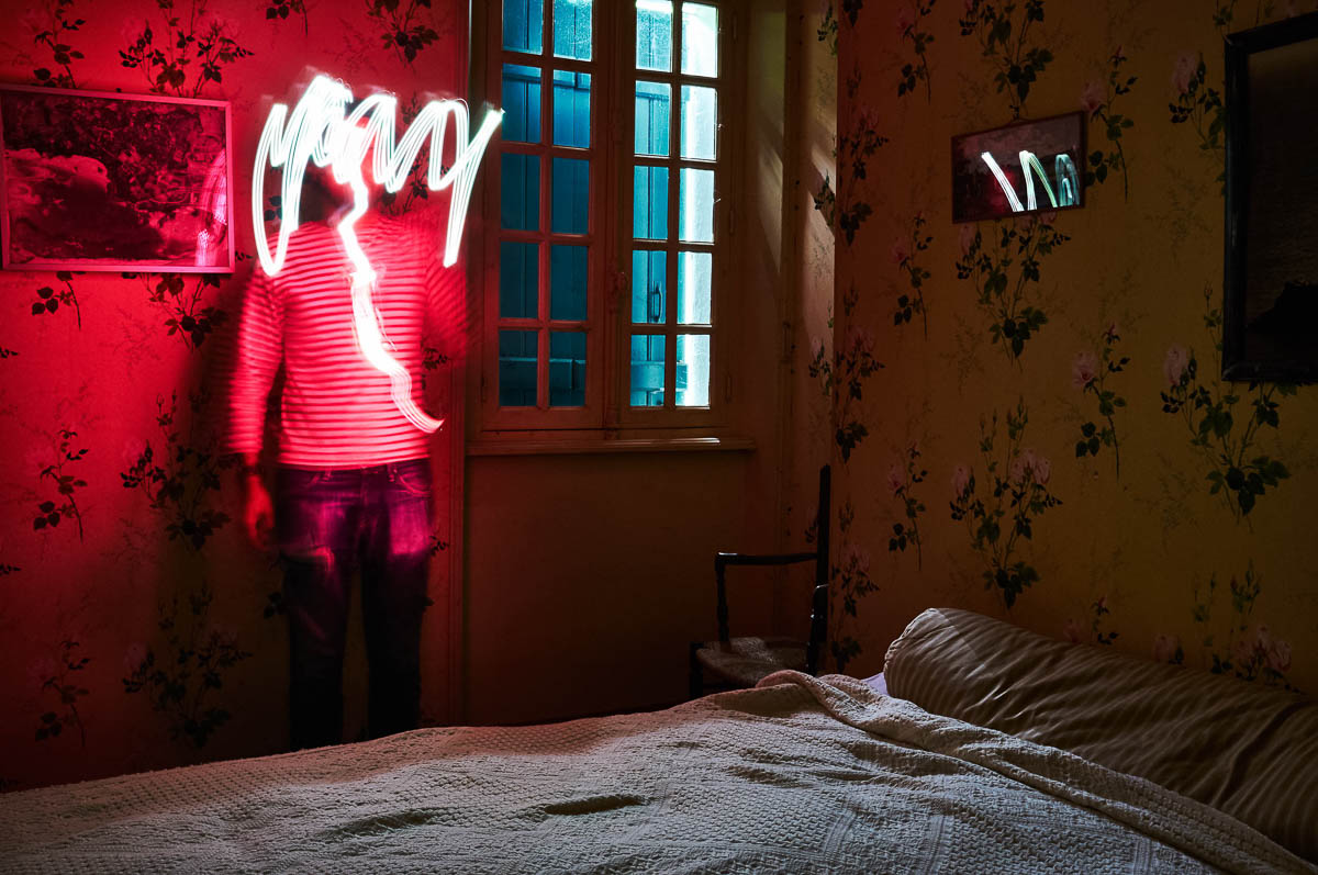 Self-portrait of Emmanuel Pineau in a vintage room, his face being concealed by a red light painting effect, from the series Out of disorders by Emmanuel Pineau