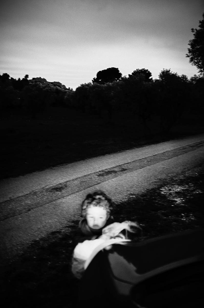 A child plays in the headlights of a car by the side of the road, from the series Out of disorders by Emmanuel Pineau